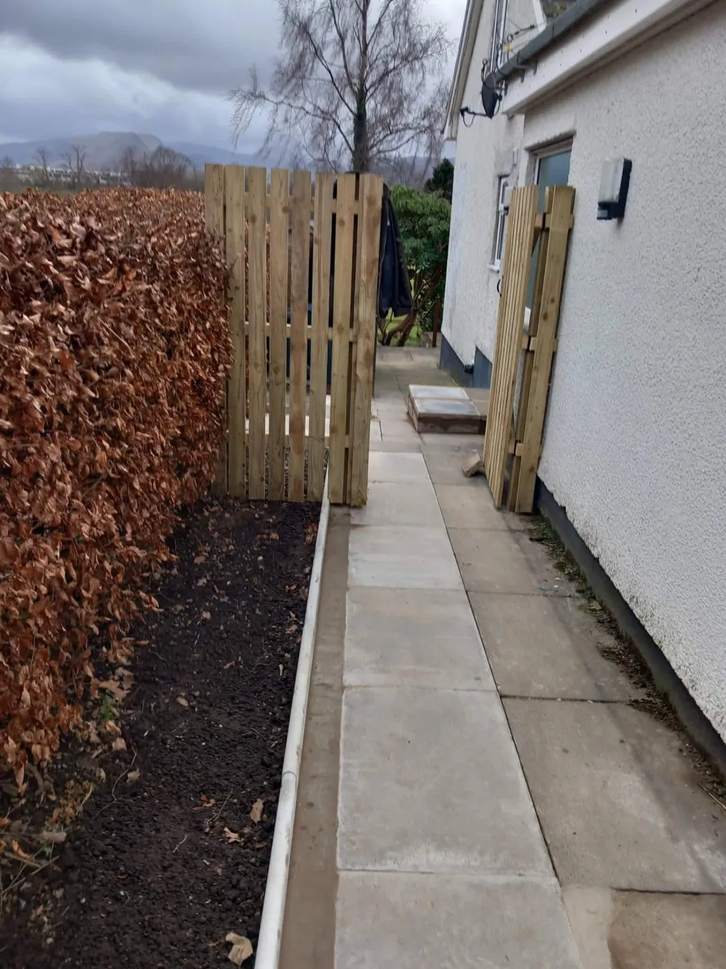 Timber fence and gate beside a concrete path next to a house
